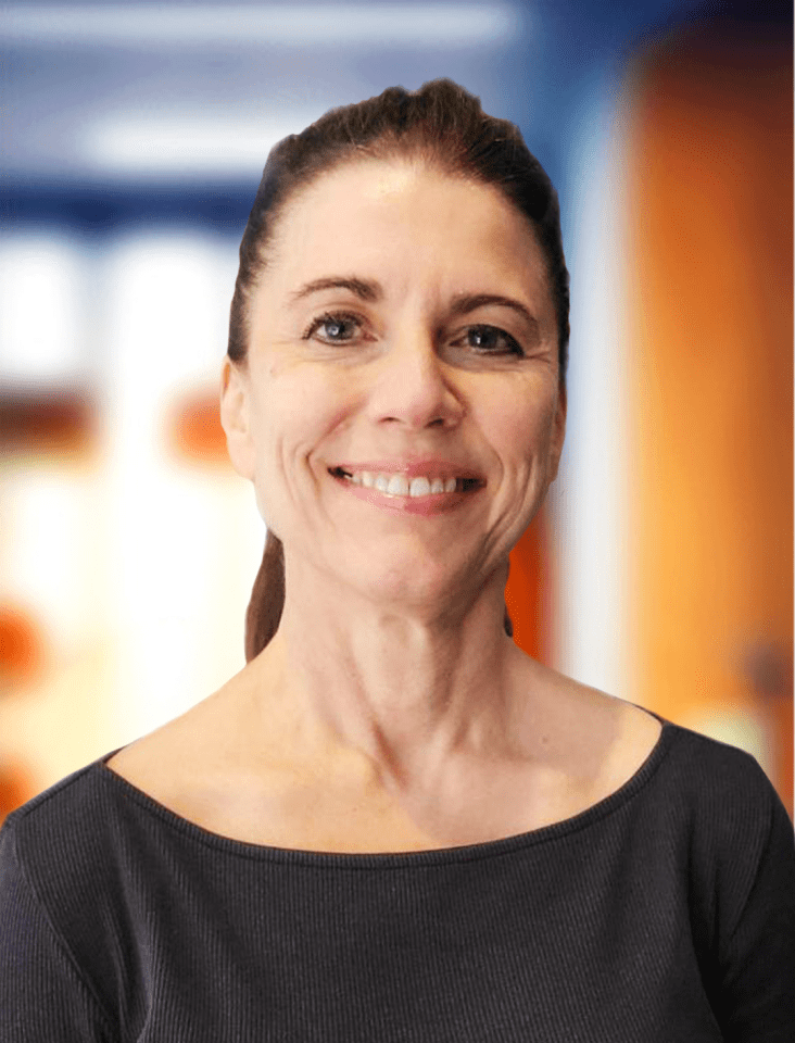 Professional headshot of Kristie Wolfe, smiling warmly. She has medium-length dark brown hair and is wearing a black sleeveless top. The background is softly blurred with blue and orange tones, keeping the focus on her face.